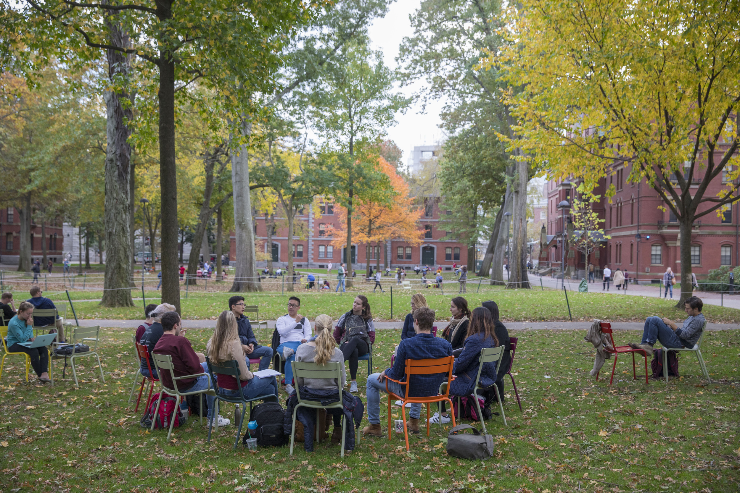 A circle of students sit in chairs in Harvard Yard.
