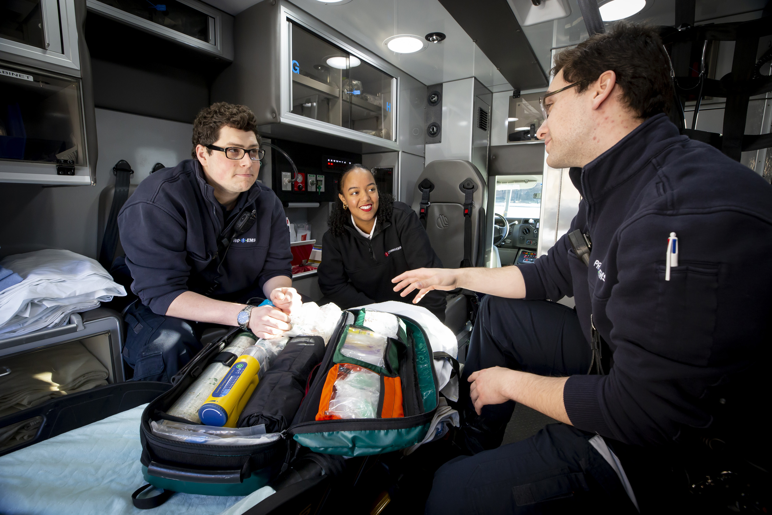 The three EMTs talk in the back of the ambulance.