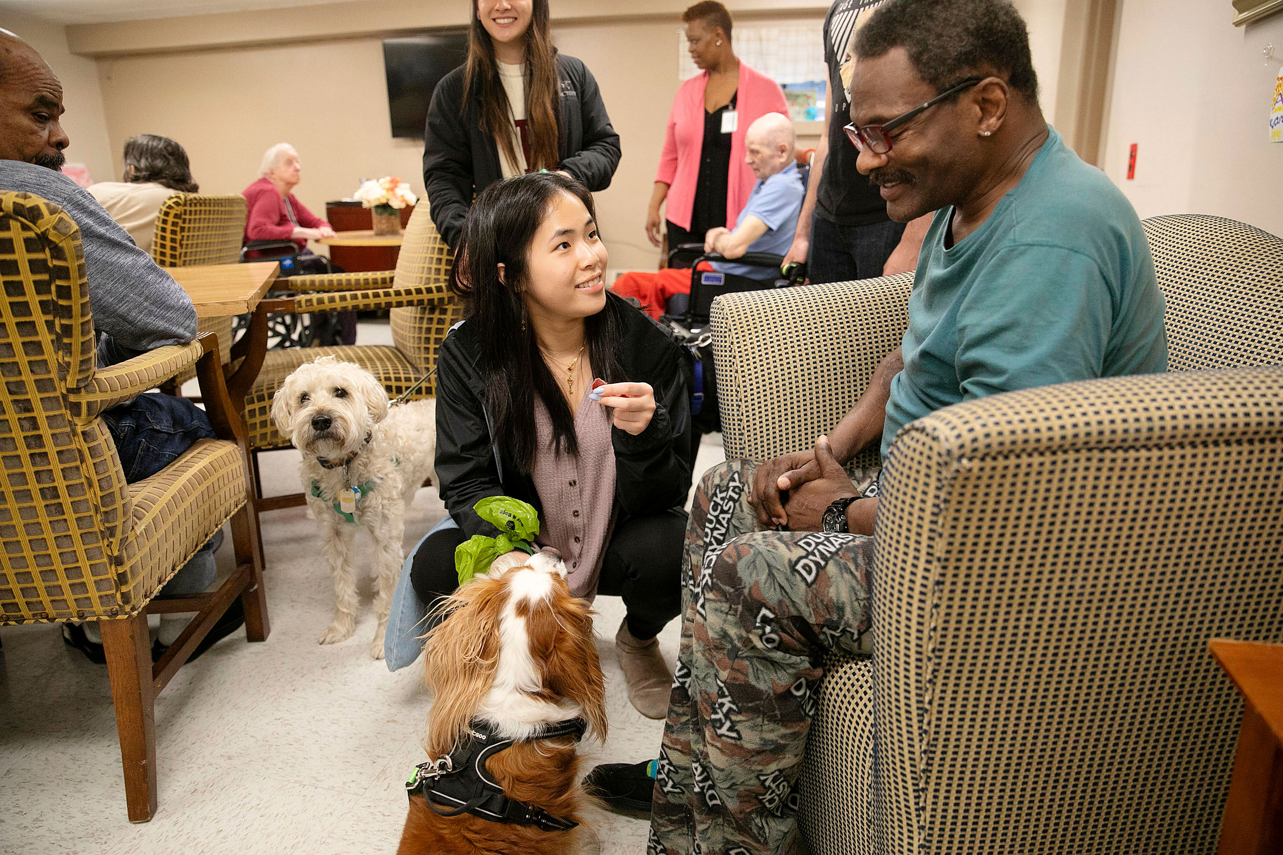 Woman feeds dog a treat with man in wheelchair.