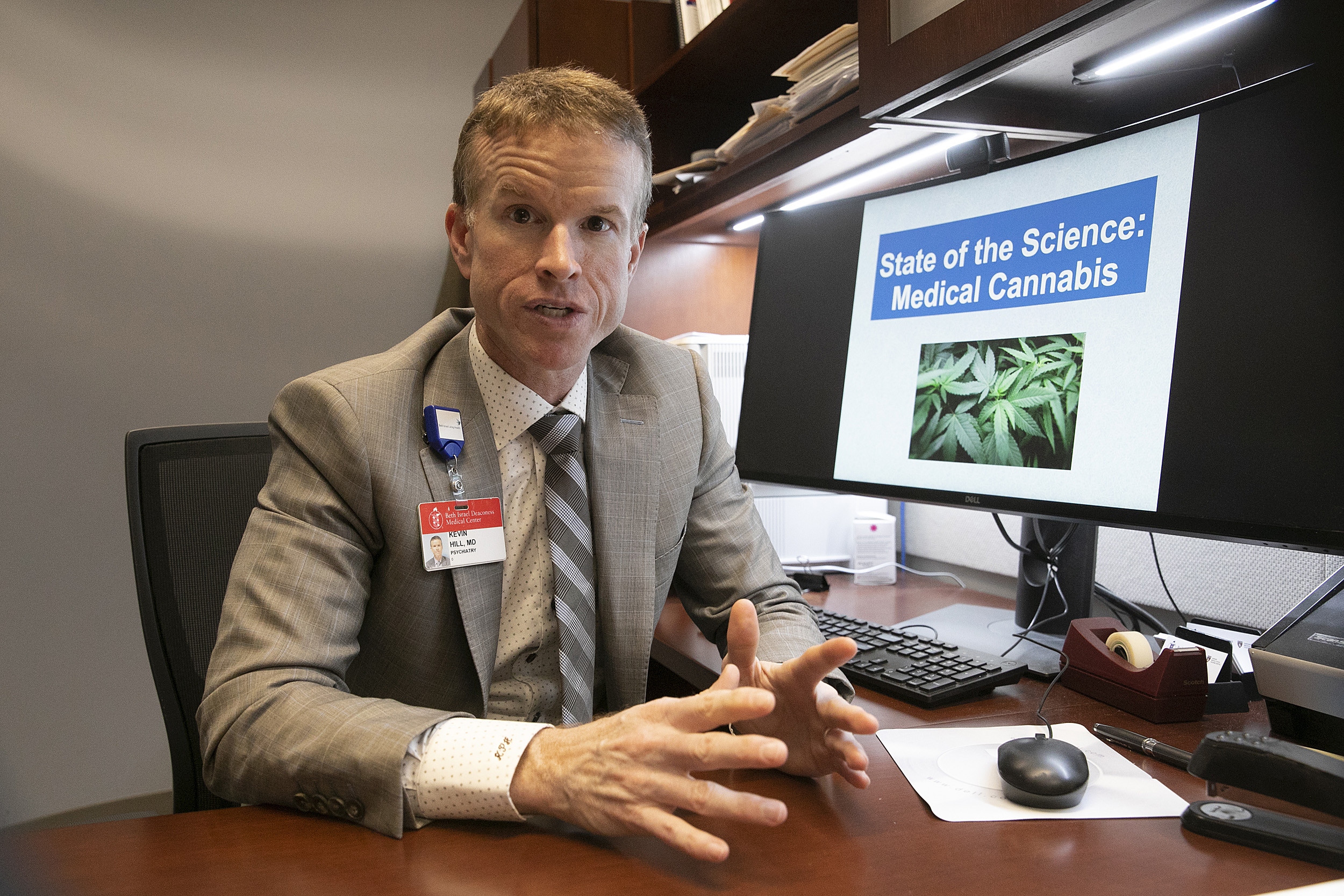 Professor sitting at desk with computer monitor showing marijuana.