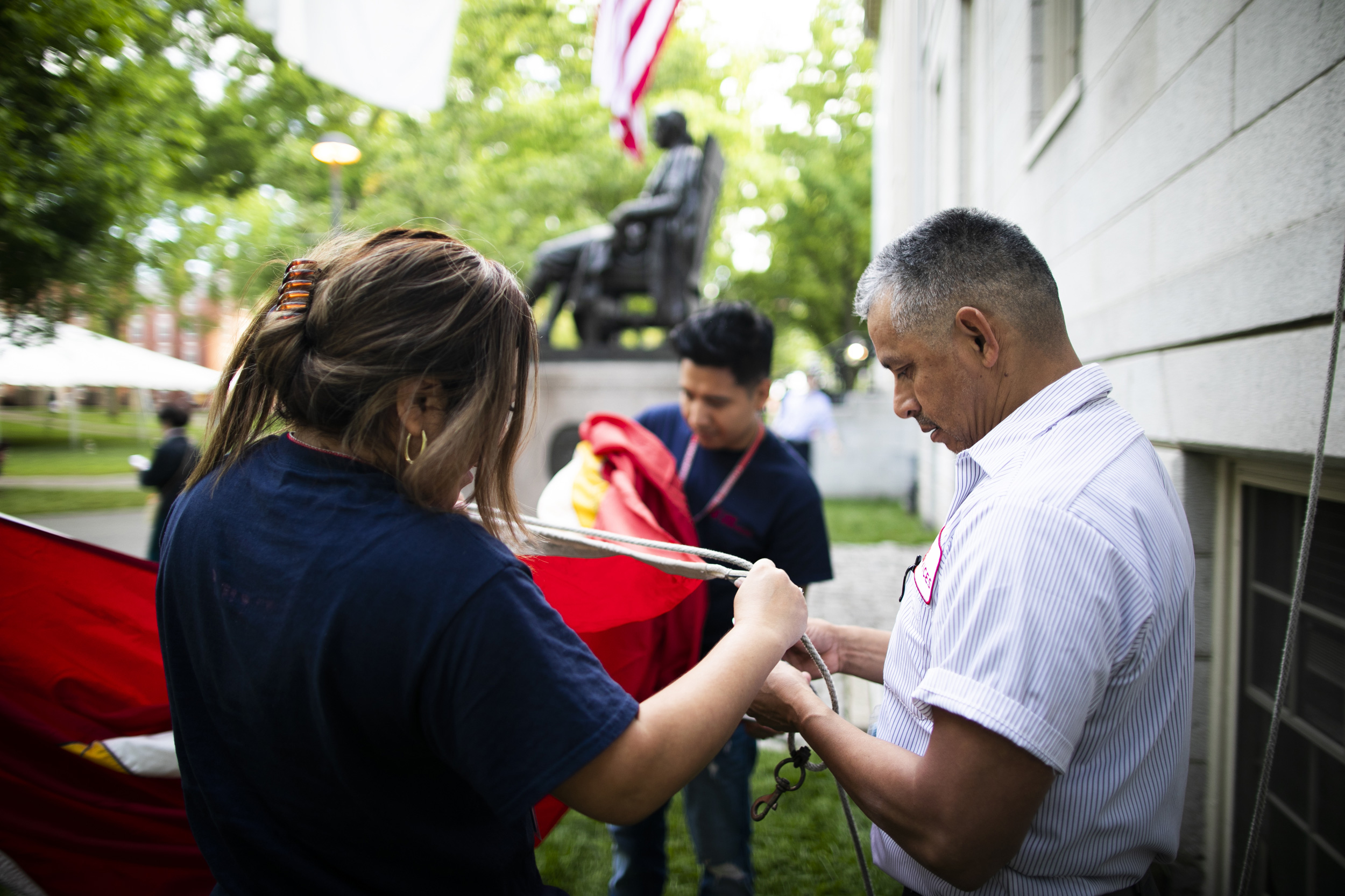 Gabriel (right) works with his colleagues to hang the Harvard veritas flag over the John Harvard Statue.