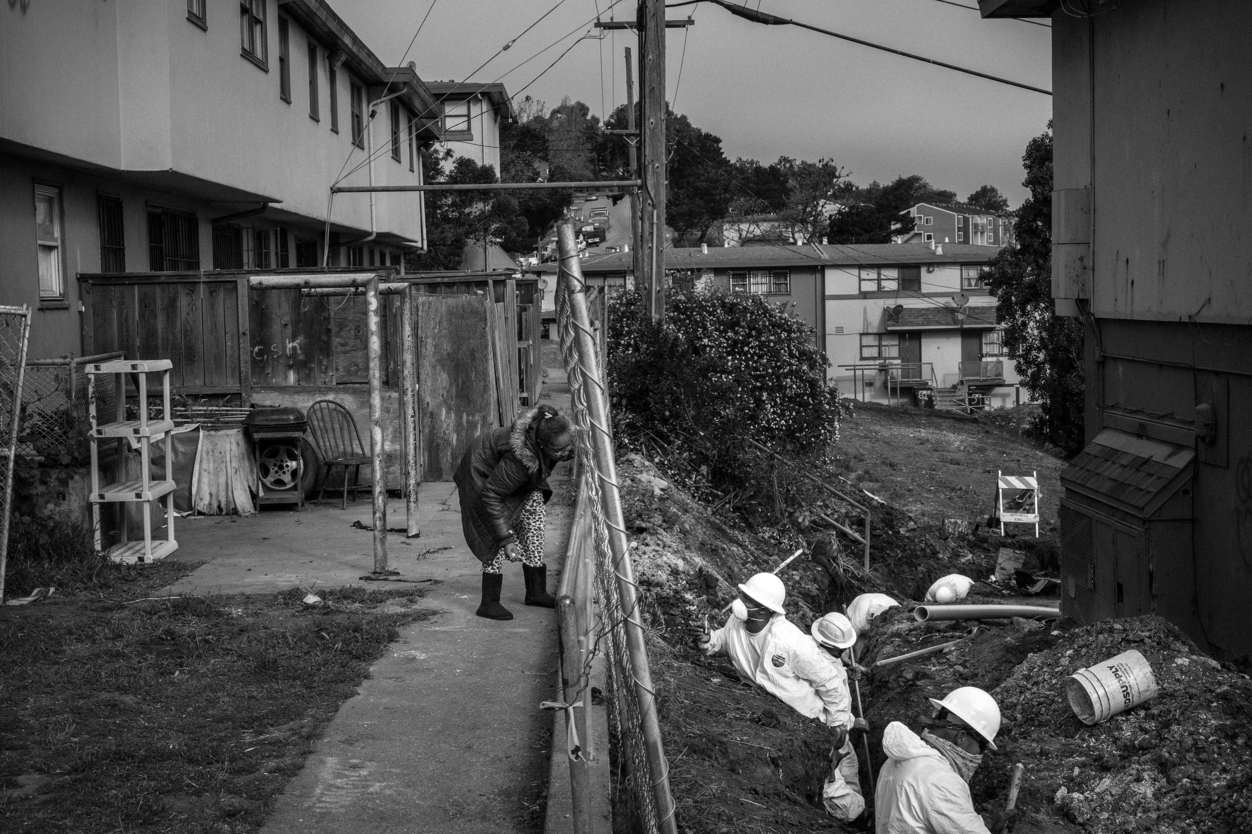 A resident talks to workers in the Hunters Point neighborhood of San Francisco, California on May 5, 2017. Safety suits and masks are worn due to high levels of nuclear contamination. The ship yards were once used to tested radiation on living organisms, and storage of boats contaminated during nuclear tests. The area also contains petroleum fuels, pesticides, heavy metals, PCBs, organic compounds and asbestos. It is one of the countries most polluted sites, and was designated a superfund site in 1989. As parts of the area are cleaned and cleared for construction, a housing company is building multi million dollar townhouses and renaming the neighborhood the San Francisco Shipyard.