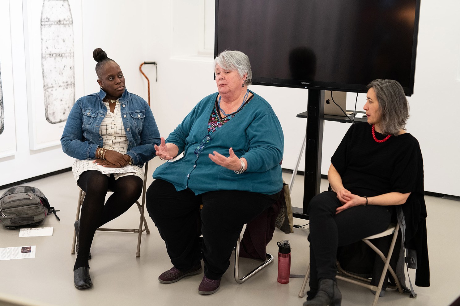 three women sitting in chairs, speaking to an audience