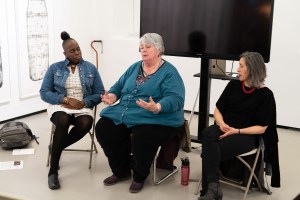 three women sitting in chairs, speaking to an audience