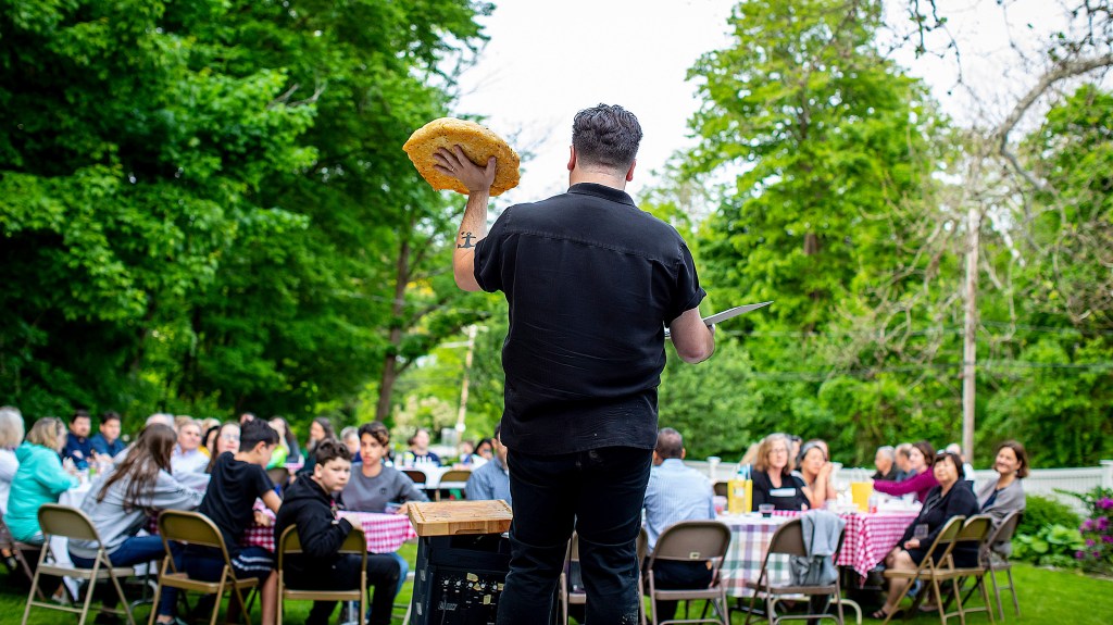 Israel Buffardi faces congregants sitting at tables outside, holding up focaccia he made for a Sacred Supper.