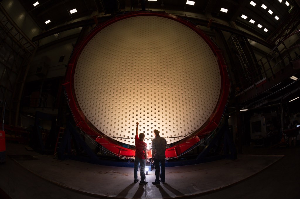 Two individuals stand in front of Magellan Mirror.