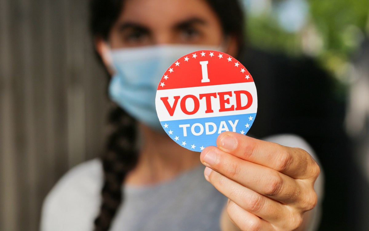 Young woman wearing face mask holding I voted today sticker.