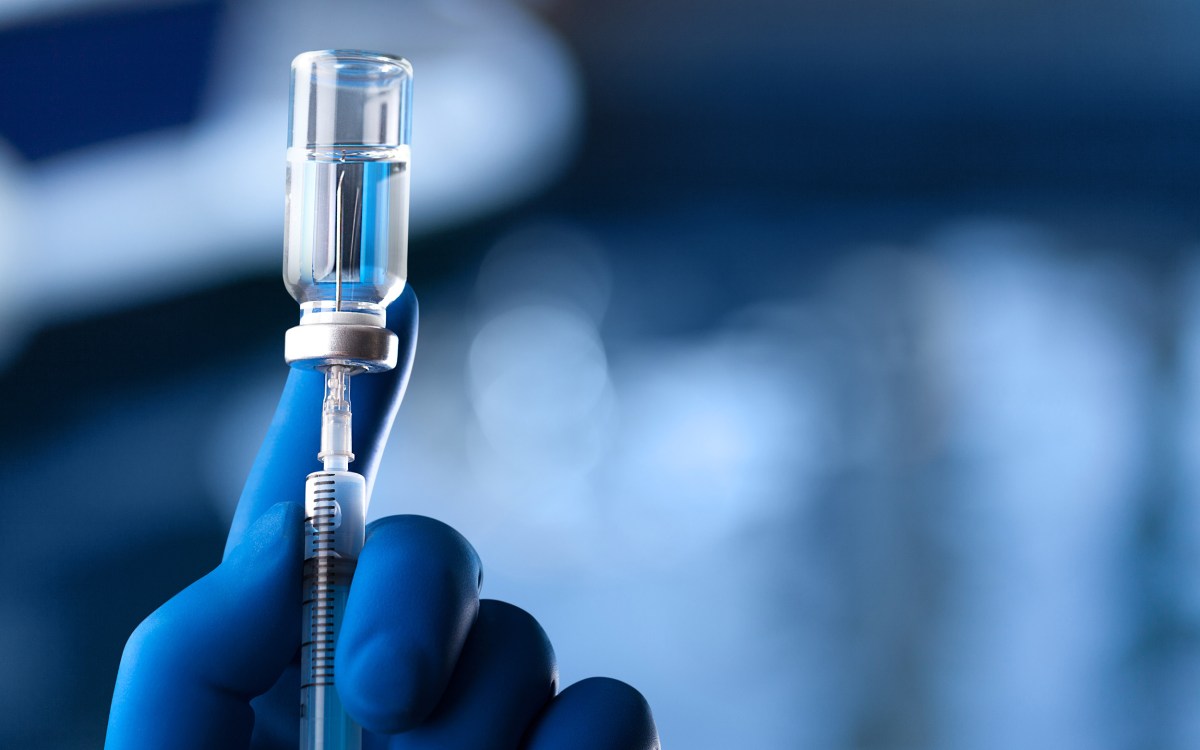 A medical hand in a glove holds an ampoule with a vaccine and a syringe with illustration