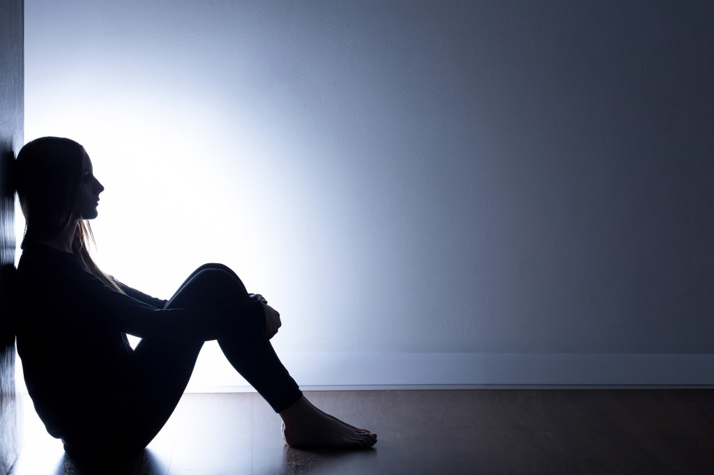 Young adult sitting alone in dark room.