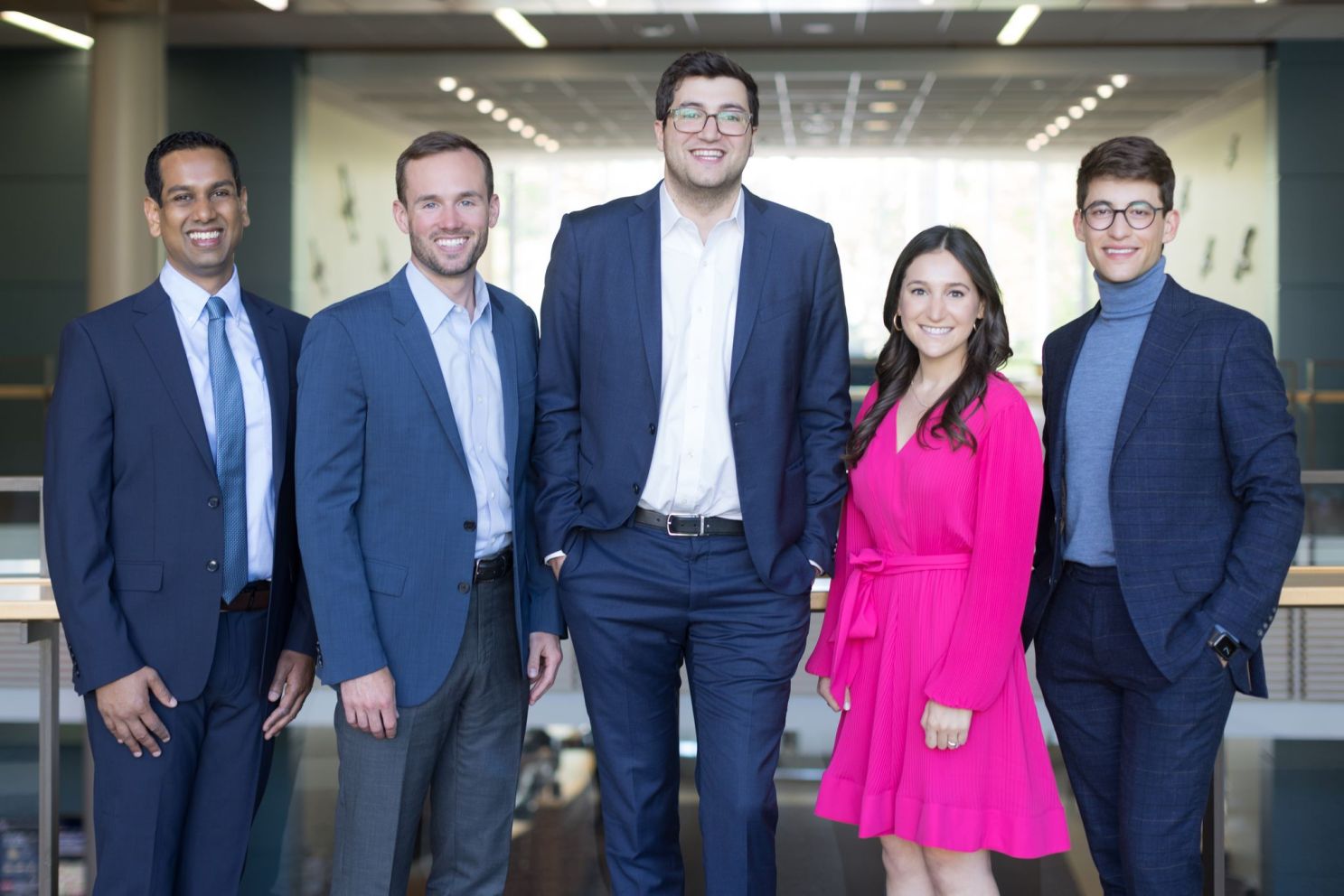 Four men in suits and a woman in a pink dress