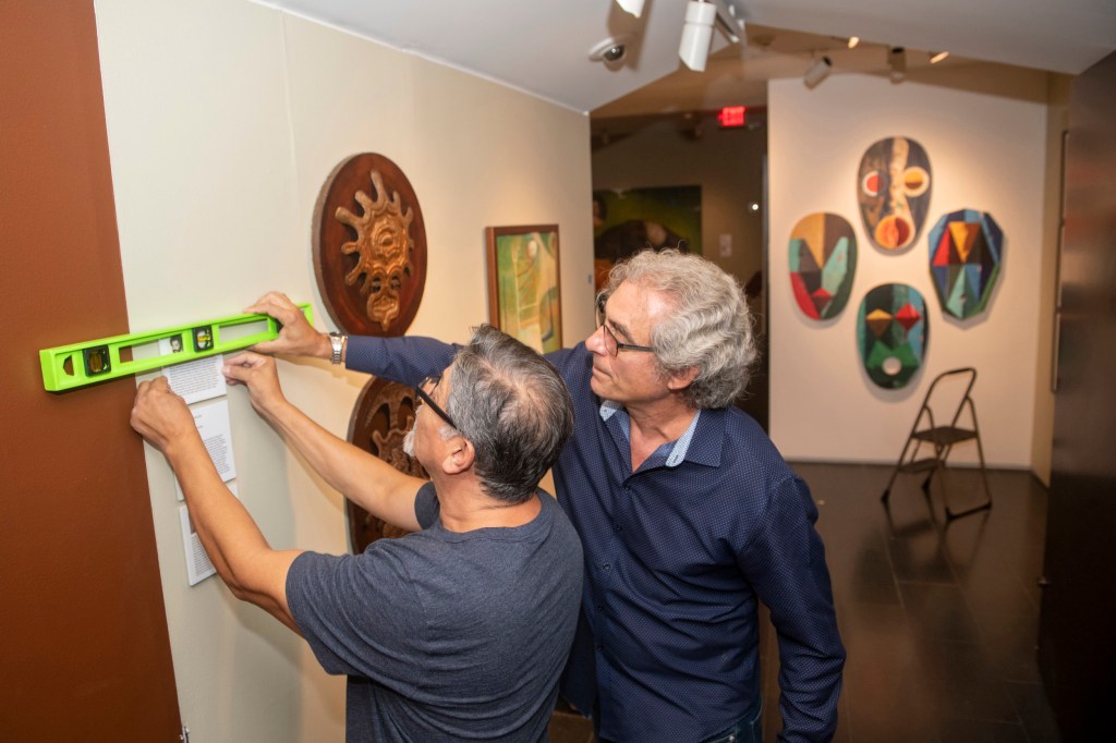 Alejandro de la Fuente and Pablo Gonzalez hang exhibition labels.