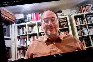 Franklin Foer wearing glasses and a button up shirt sitting in front of a bookcase.