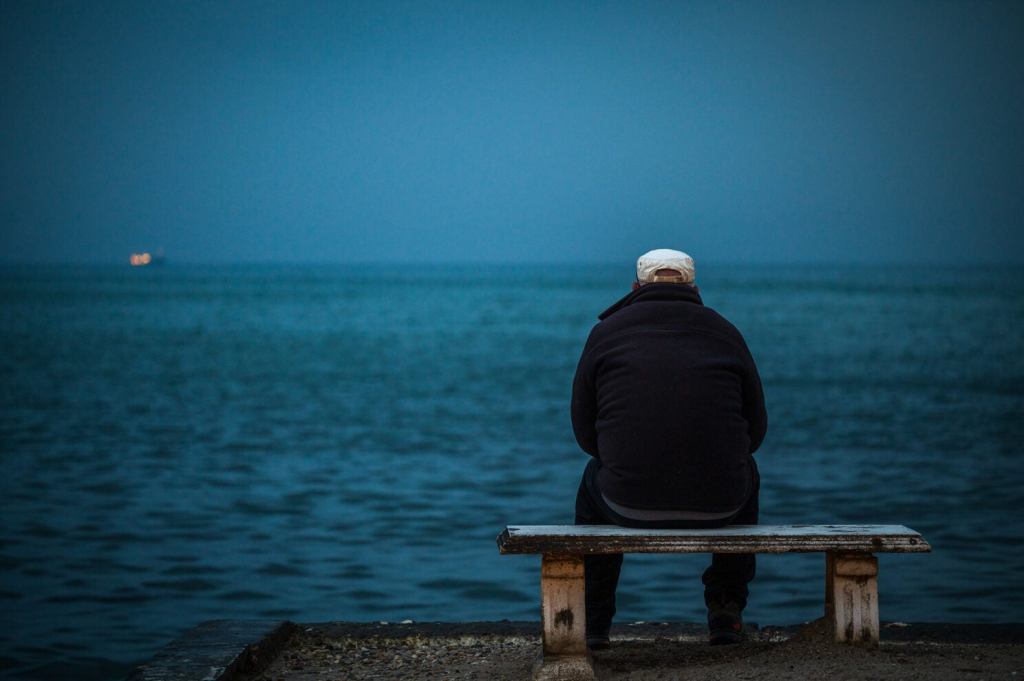 Lonely person sits alone on a bench looking at the ocean.