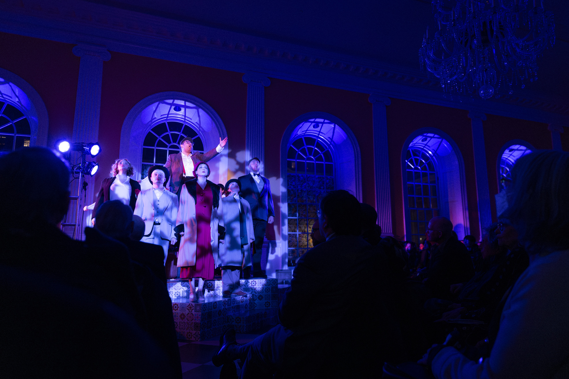 Audience members look on as the cast performs a dramatic moment.