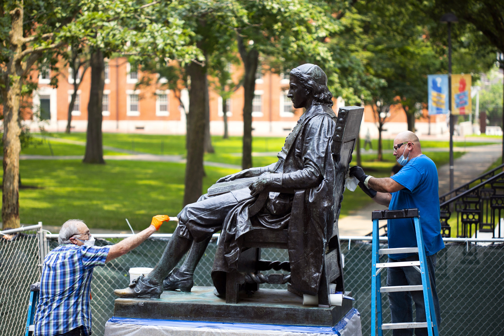 Robert Shure and Noe Magana restore the John Harvard Statue in Harvard Yard.