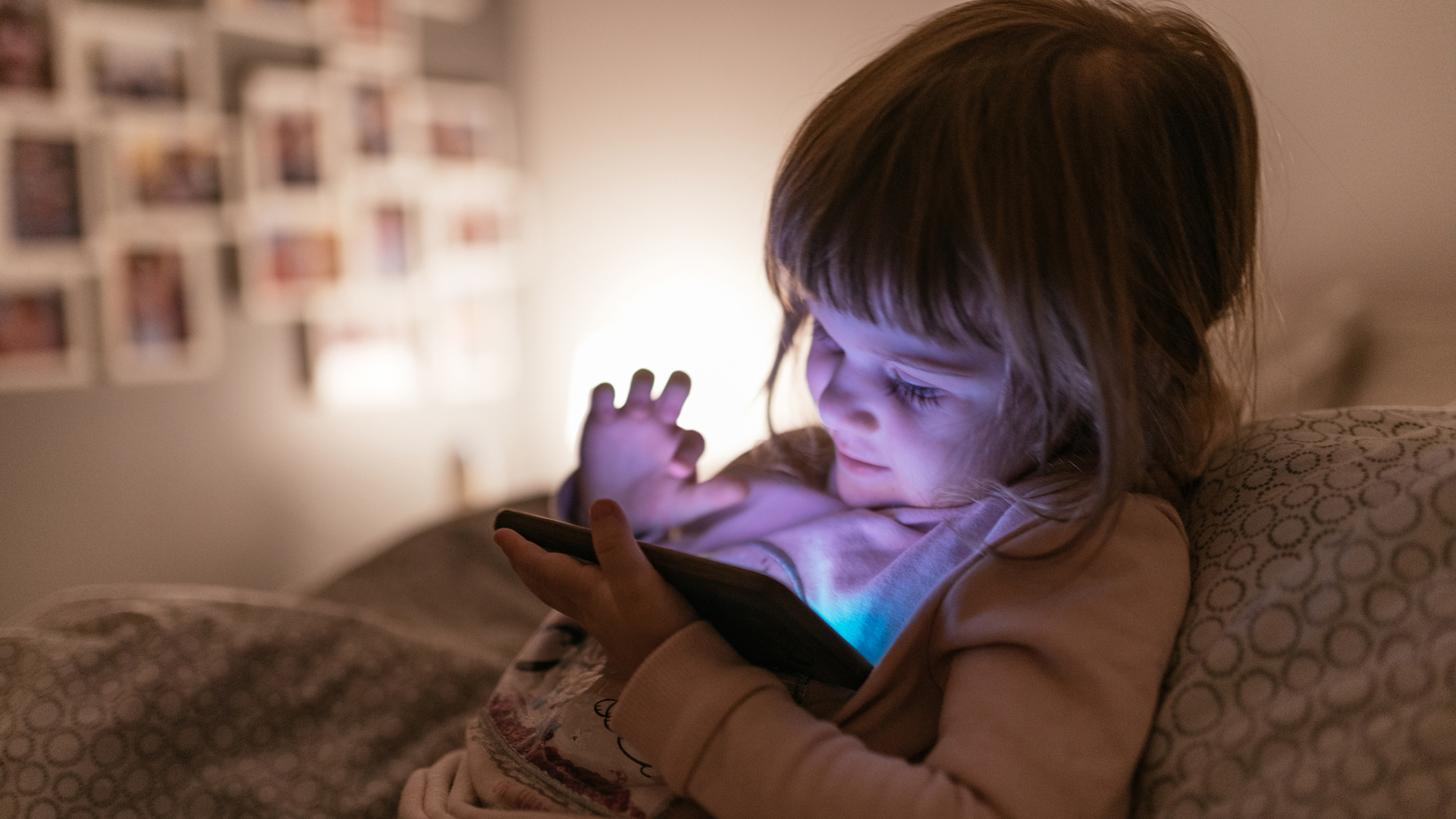 A child  sits up in bed and plays on a cell phone.
