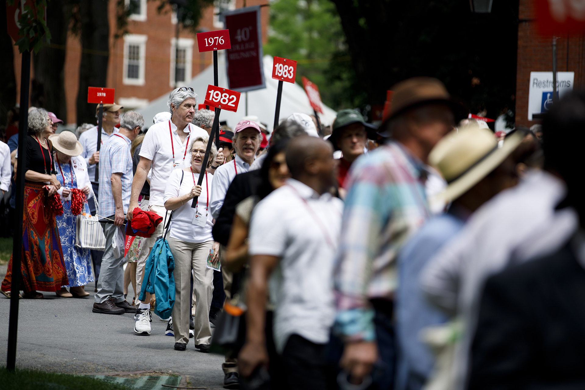 Alumni holding signs with their year file into Harvard Yard.