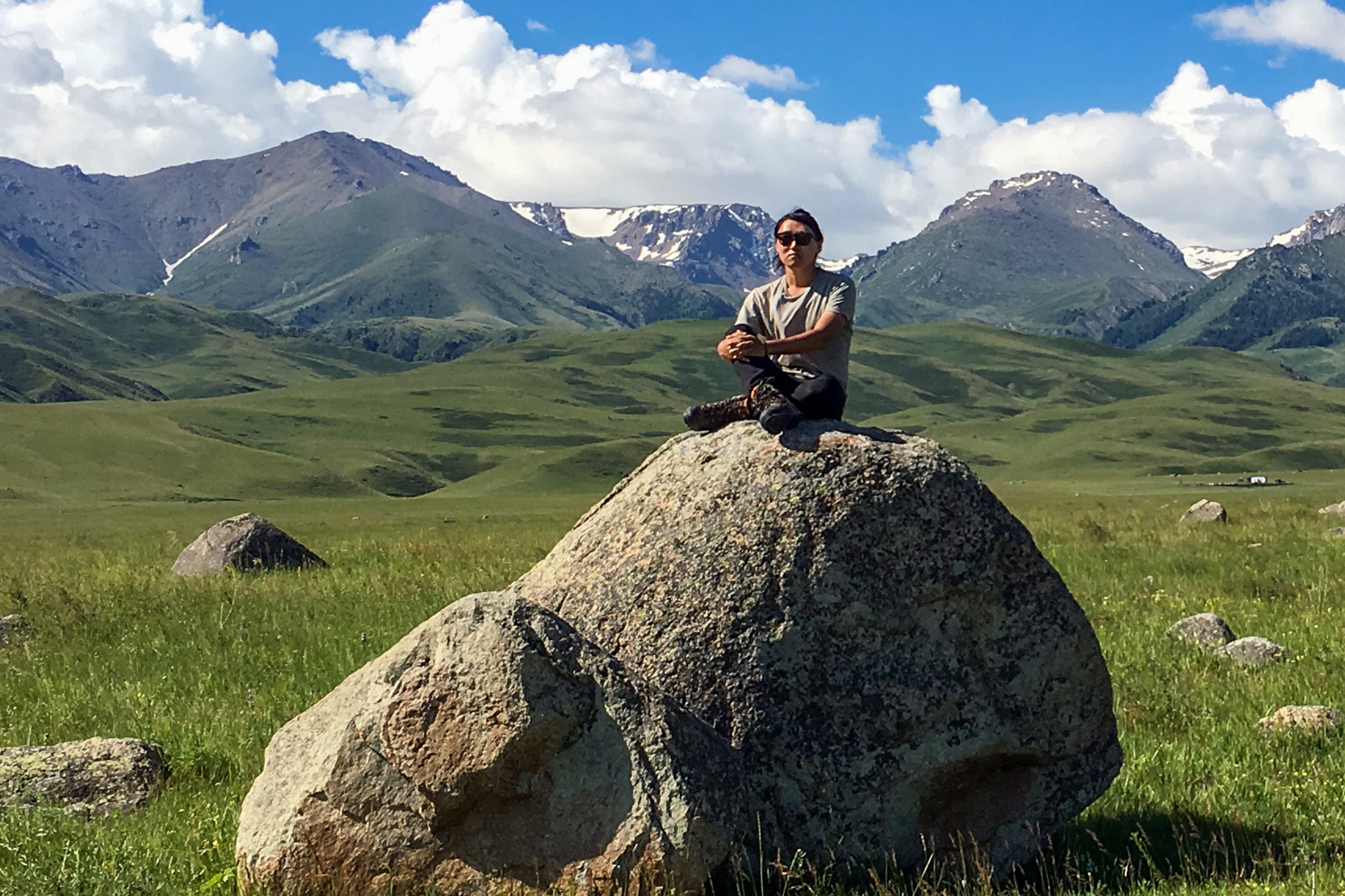 Alexander Mee-Woong Kim sitting on a rock with mountains in background, in Kazakhstan.