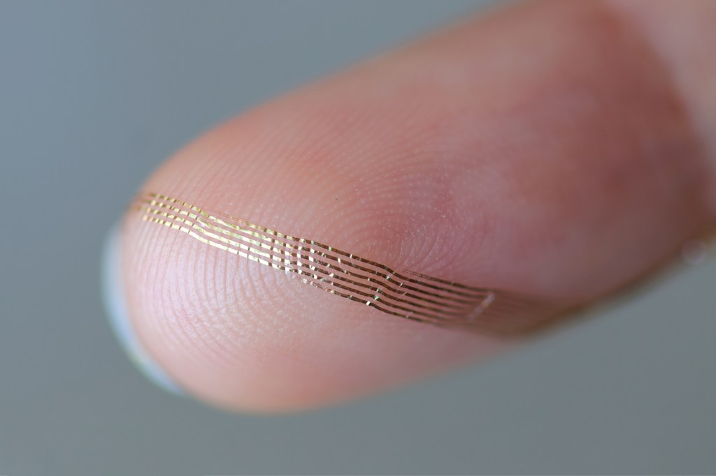 Axoft's flexible neural probe is displayed on a finger tip for perspective.