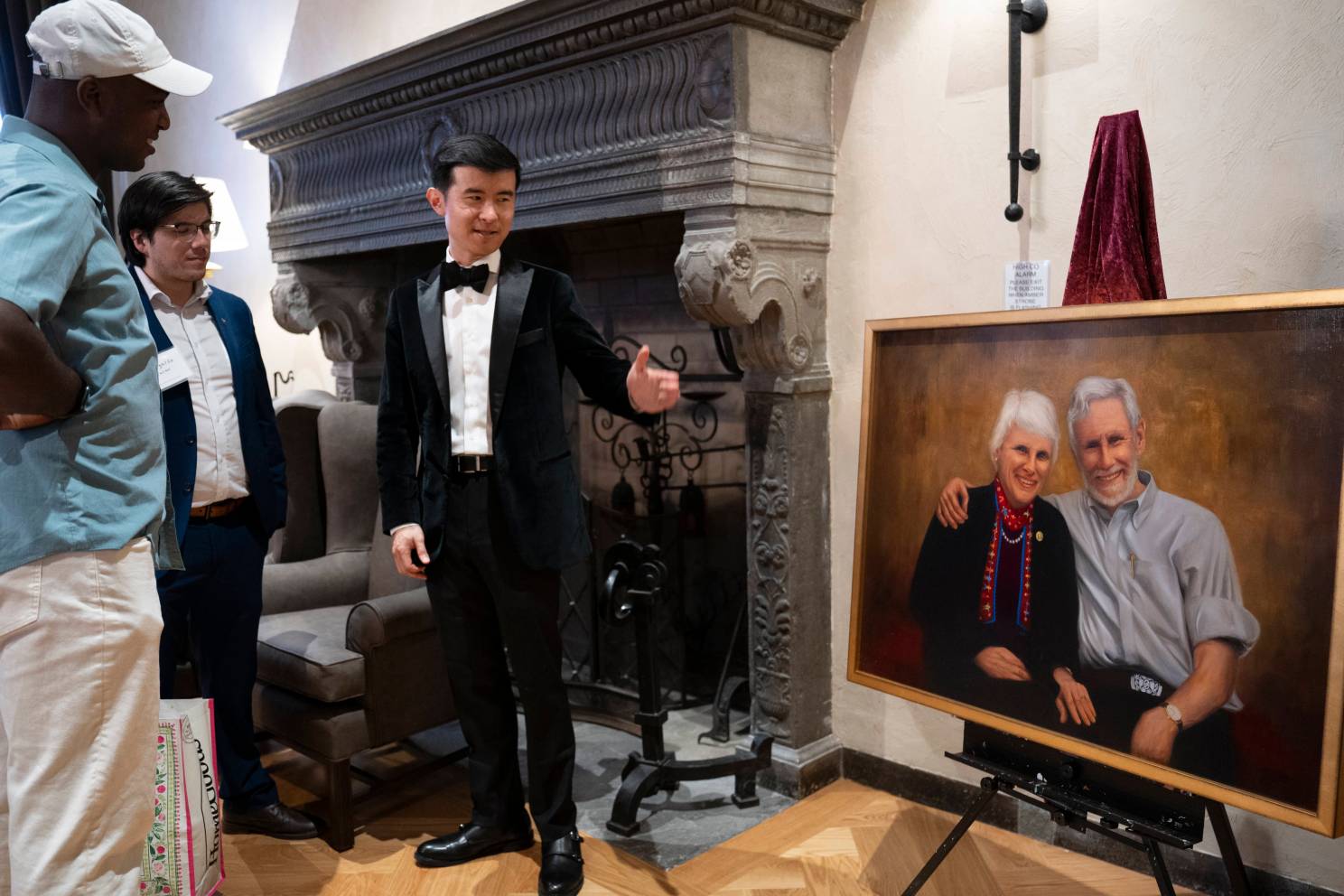 A portrait of former Adams House Faculty Deans Judith and John Palfrey ’67 by artist William Shen, ’22 (center). Shen speaks with Chukwudi Ilozue ’25 and Harvard Medical School student Eduardo Duran.
