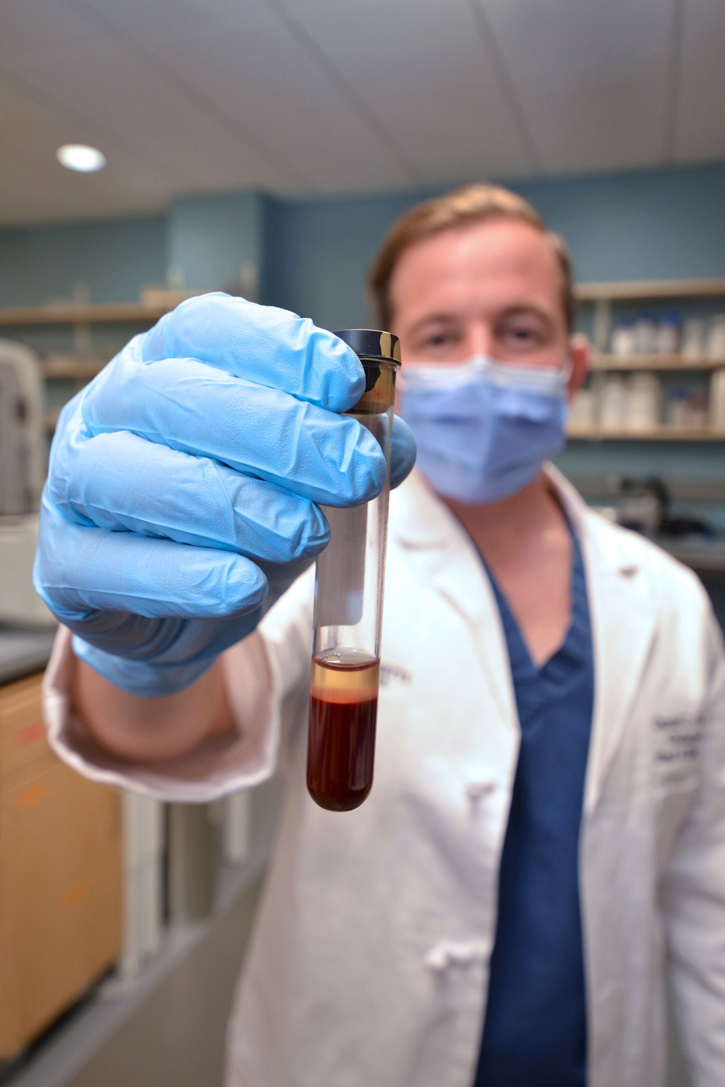 Daniel Faden holding up a vial of blood in his lab at Mass Eye and Ear. 
