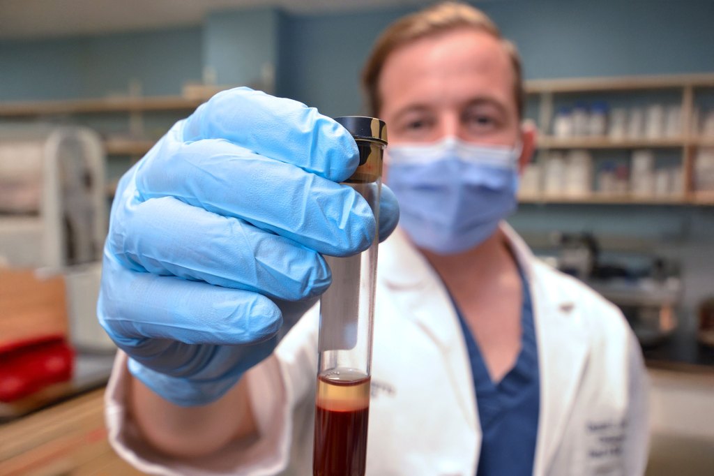 Daniel Faden holding up a vial of blood in his lab at Mass Eye and Ear.
