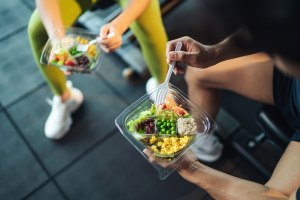 Man and woman healthy eating salad after exercise at fitness gym.
