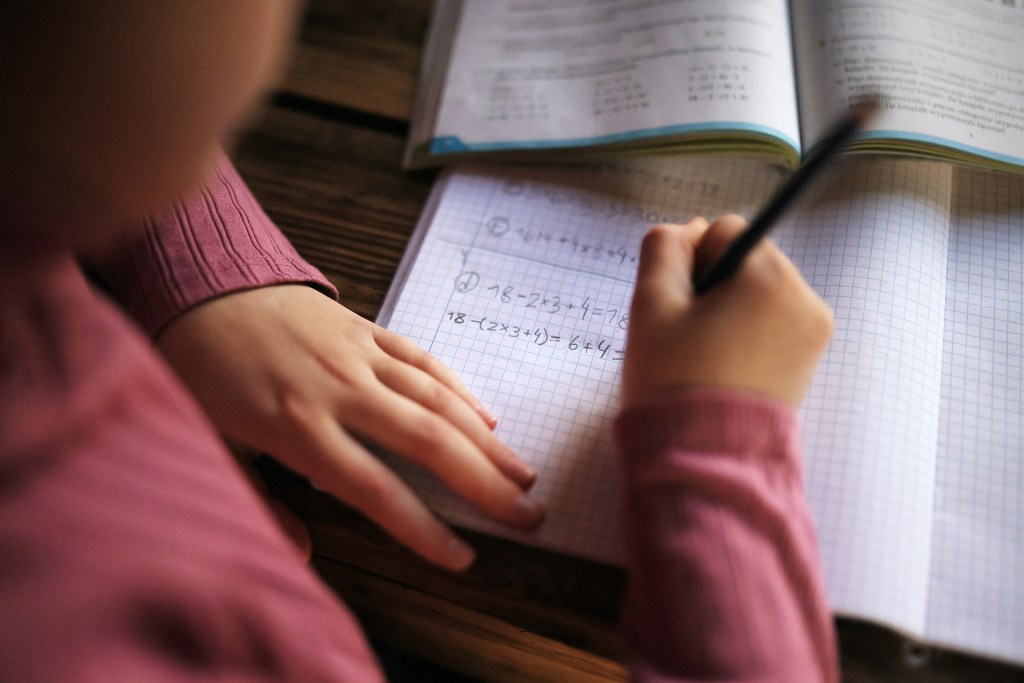 Close-up view on student's hand doing math homework in notebook.