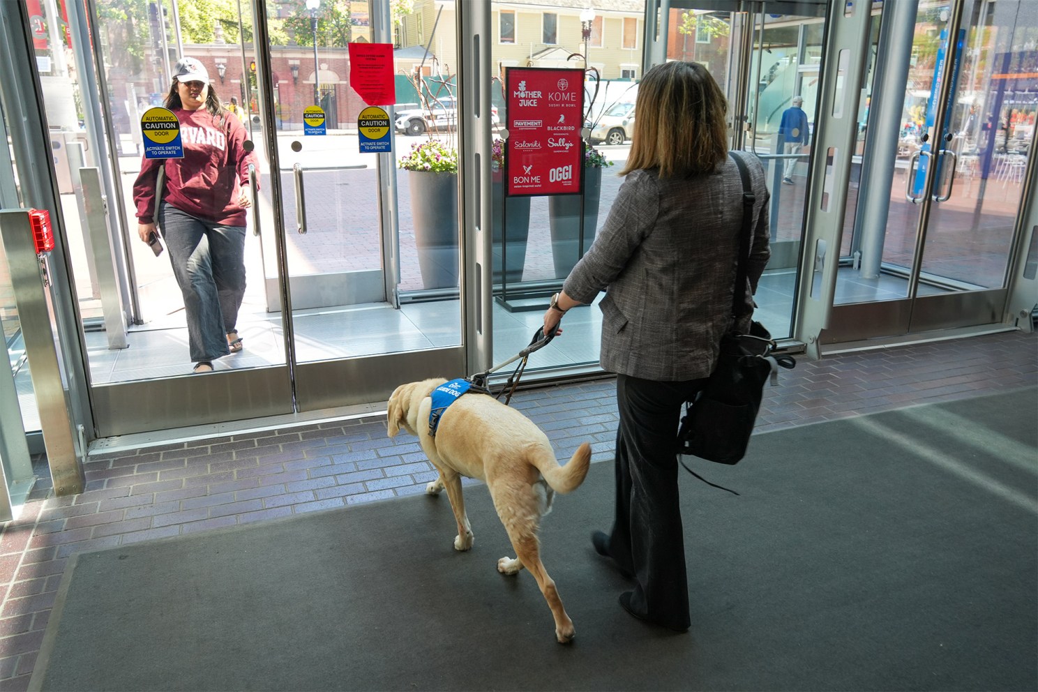 Woman with back to camera, accompanied by service animal, walking toward door of Smith Campus Center.