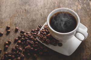 A steaming cup of coffee with coffee beans