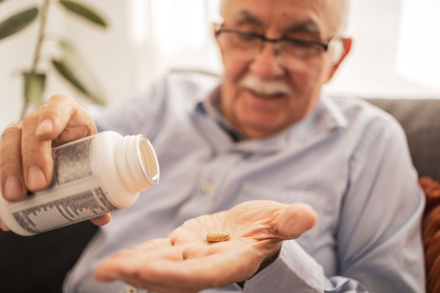 Elderly man holding a supplement pill in his palm.